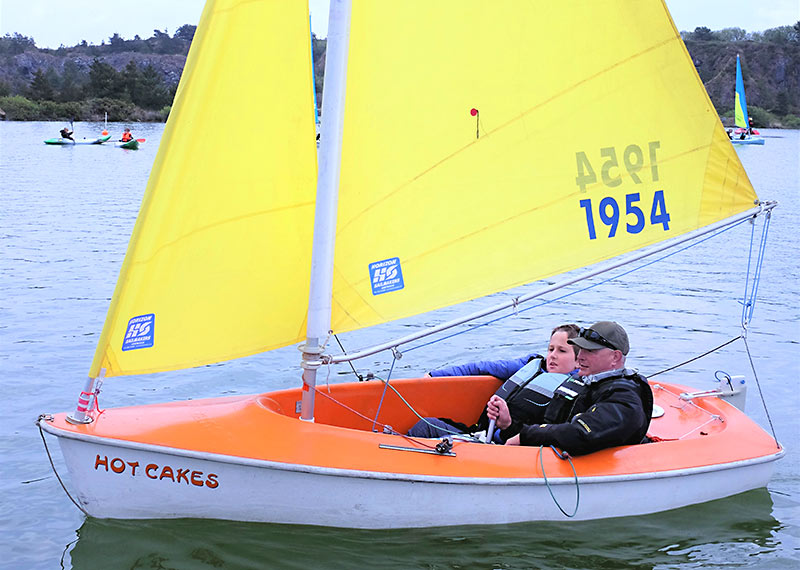 A young disabled lad sails in an accessible dinghy with an instructor supporting him