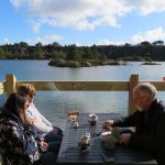 Three people have coffee and cake on the waterside deck of the Trevassack cafe with CST