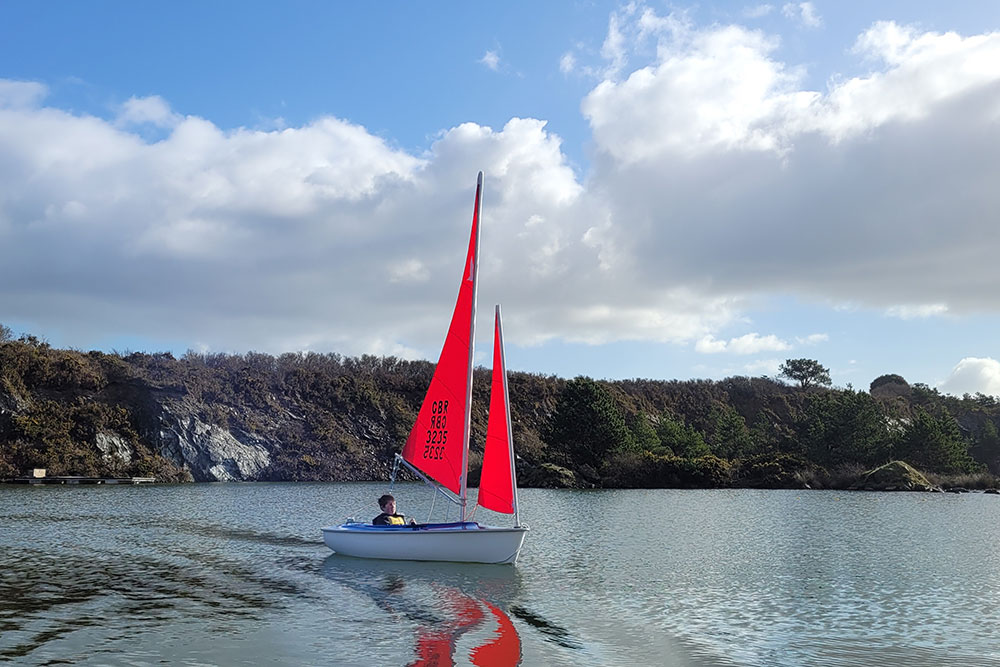 Bright red sails of an accessible hansa dinghy driven by a child on trevassack lake