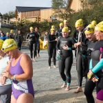 A group of swimmers in wetsuits and yellow swimming caps prepare to Lap the Lake