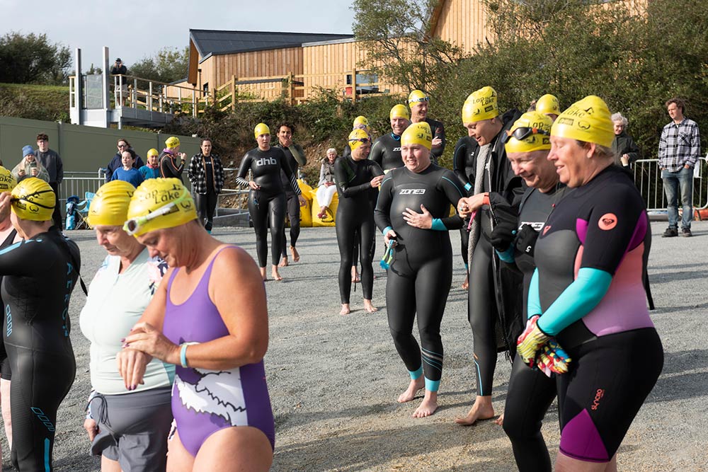 A group of swimmers in wetsuits and yellow swimming caps prepare to Lap the Lake
