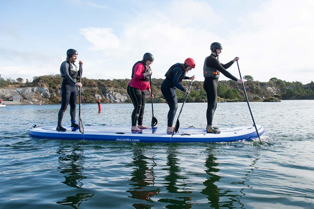 Four adults paddleboard as a team